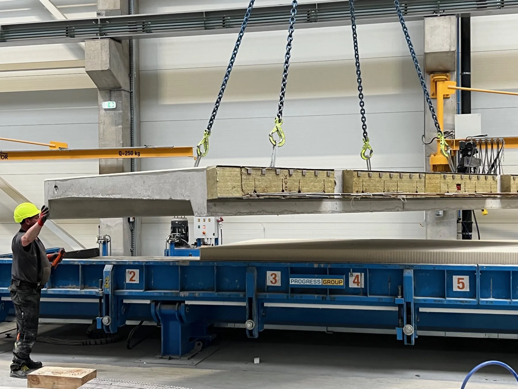 Prefabrykowana płyta balkonowa zdejmowana z formy suwnicą w hali produkcyjnej Formee, z widoczną wkładką izolacyjną na krawędzi